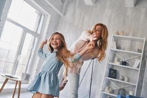 spensierato tempo insieme. madre e figlia Tenere mani e sorridente mentre danza nel Camera da letto foto