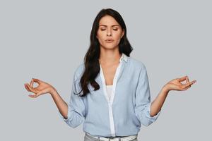 zen. attraente giovane donna Meditare e conservazione occhi chiuso mentre in piedi contro grigio sfondo foto