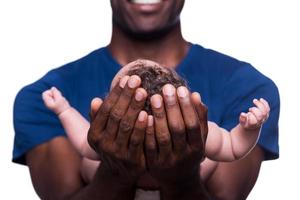 nuovo vita nel il suo mani. avvicinamento di contento giovane africano uomo Tenere il suo poco bambino e sorridente mentre in piedi isolato su bianca foto