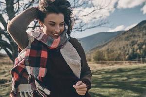 pieno di vita energia. attraente giovane donna sorridente e conservazione mano nel capelli mentre in esecuzione su il valle nel montagne all'aperto foto