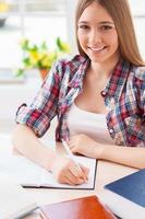 io amore studiando. superiore Visualizza di allegro adolescenziale ragazza studiando mentre seduta a il scrivania foto