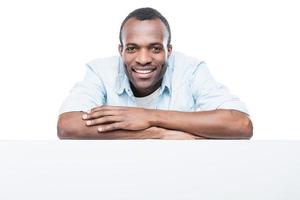 affascinante bello. bello africano uomo nel blu camicia pendente a copia spazio e sorridente mentre in piedi contro bianca sfondo foto