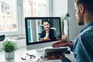 grave giovane uomo parlando per collega di video chiamata mentre seduta nel ufficio foto