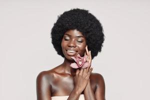 ritratto di bellissimo giovane africano donna Tenere fiore vicino viso e sorridente foto
