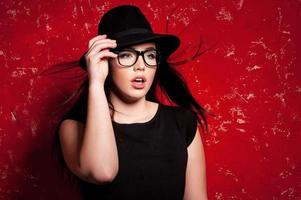 fascino moda modello. bellissimo giovane donna nel cappello e bicchieri in posa contro rosso sfondo foto