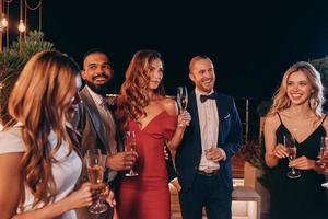 gruppo di bellissimo persone nel vestito formale comunicare e sorridente mentre la spesa tempo su lusso festa foto