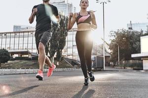 godendo bene correre. giovane coppia nel sport capi di abbigliamento in esecuzione attraverso il città strada insieme foto