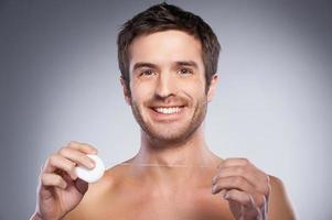 uomo con dentale filo interdentale. ritratto di bello giovane A petto nudo uomo Tenere dentale filo e sorridente mentre isolato su grigio sfondo foto