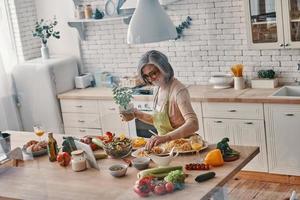 superiore Visualizza di anziano donna nel grembiule cucinando salutare cena mentre la spesa tempo a casa foto