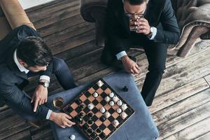 chi è andando per vincere superiore Visualizza di giovane riflessivo uomini nel pieno tute giocando scacchi mentre seduta in casa foto