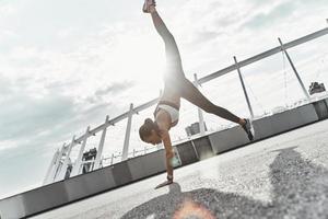 mondo sottosopra fuori uso. pieno lunghezza di moderno giovane donna nel gli sport capi di abbigliamento fare handstand mentre esercizio all'aperto foto