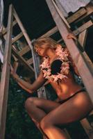 bellissima bellezza. attraente giovane donna indossare hawaiano lei e sorridente mentre seduta su il di legno passaggi foto
