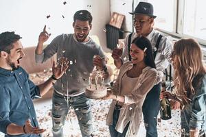 tempo per un' compleanno torta. superiore Visualizza di contento giovane uomo festeggiare compleanno tra amici mentre in piedi nel camera con coriandoli volante in giro foto