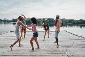 giovane e gratuito. pieno lunghezza di giovane persone nel casuale indossare sorridente e Esprimere a gesti mentre godendo spiaggia festa foto