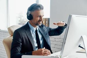 contento uomo d'affari nel cuffie avendo ragnatela conferenza mentre seduta a il suo Lavorando posto foto