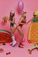 permettere il festa iniziato pieno lunghezza di Due giovane donne nel costumi da bagno copertura facce con palloncini mentre in piedi contro rosa sfondo foto