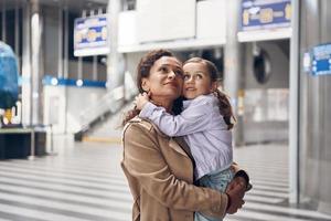 bellissimo maturo donna trasporto sua poco figlia e guardare lontano mentre in piedi a aeroporto terminale foto