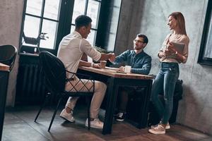 giovane moderno colleghi nel inteligente casuale indossare tremante mani e sorridente mentre Lavorando nel ufficio foto