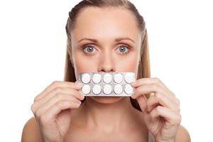 donna con medicine. pacchetto colpito della tenuta della giovane donna delle pillole davanti alla sua bocca mentre stando isolato su bianco foto
