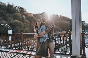 romantico momento. bello uomo Abbracciare una persona giovane attraente donna mentre in piedi su il ponte all'aperto foto