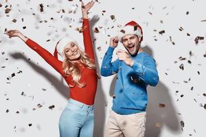 Natale festa. bellissimo giovane coppia nel Natale cappelli Esprimere a gesti e sorridente mentre in piedi contro grigio sfondo foto