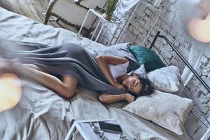 tranquillo, calmo dormire. superiore Visualizza di attraente giovane donna coperto con coperta conservazione occhi chiuso e sorridente mentre dire bugie su il letto a casa foto