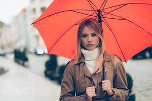 donna con ombrello. attraente giovane donna trasporto ombrello e guardare a telecamera mentre in piedi su il strada foto