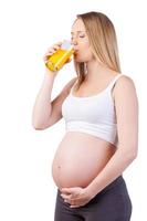 potabile fresco succo. bellissimo incinta donna potabile arancia succo mentre in piedi isolato su bianca foto