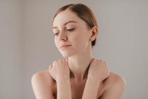 calma e rilassato. ritratto di attraente giovane donna con lentiggini su viso guardare lontano e conservazione mani su le spalle mentre in piedi contro grigio sfondo foto