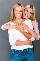 famiglia obbligazioni. sorridente giovane donna Abbracciare una persona sua madre mentre tutti e due in piedi contro grigio sfondo foto