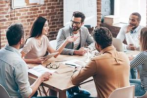 prendere grandi decisioni. giovane bella donna che gesticola e discute qualcosa con un sorriso mentre i suoi colleghi la ascoltano seduta al tavolo dell'ufficio foto