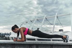 all'aperto allenamento. moderno giovane donna nel gli sport capi di abbigliamento conservazione tavola posizione mentre esercizio all'aperto foto