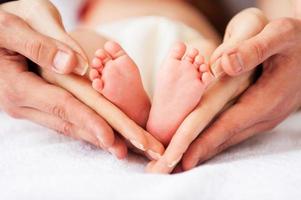 noi siamo famiglia. avvicinamento di genitori Tenere il minuscolo piedi di loro poco bambino foto