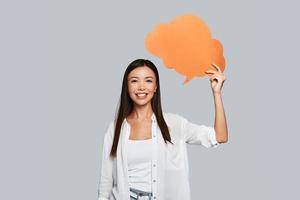 creatività nel azione. bellissimo giovane asiatico donna guardare a telecamera e sorridente mentre in piedi contro grigio sfondo foto