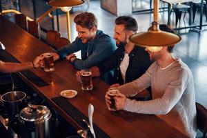 superiore Visualizza di barista servendo birra per giovane uomini mentre in piedi a il bar contatore nel pub foto