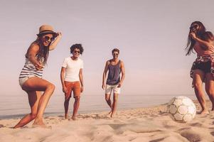 spiaggia divertimento. gruppo di allegro giovane persone giocando con calcio palla su il spiaggia foto