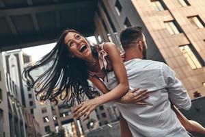 sensazione giocoso. bellissimo giovane donna conservazione bocca Aperto mentre sua fidanzato trasporto sua all'aperto foto