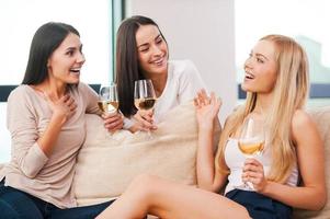 discutere il ultimo pettegolezzi. tre bellissimo giovane donne parlando e sorridente mentre potabile vino e seduta su il divano insieme foto