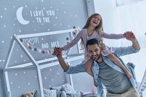 sensazione sicuro con papà. giovane padre trasporto il suo figlia su le spalle e sorridente mentre la spesa gratuito tempo a casa foto