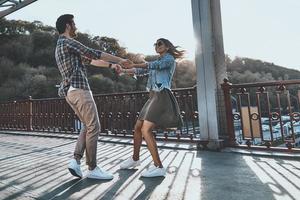 Due cuori pieno di amore. pieno lunghezza di bellissimo giovane coppia Tenere mani e Filatura mentre in piedi su il ponte all'aperto foto