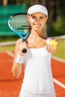 il tuo servire. bellissimo giovane donna nel gli sport capi di abbigliamento Tenere tennis racchetta e sorridente foto