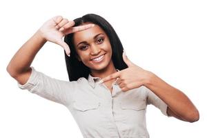 messa a fuoco su me sorridente giovane africano donna Esprimere a gesti dito telaio e sorridente mentre in piedi contro bianca sfondo foto