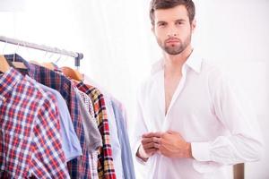 elegante e eleganza. bello giovane uomo condimento su bianca camicia e guardare a telecamera foto