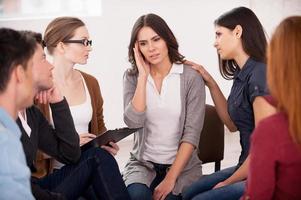 raccontare noi di il tuo problema depresso giovane donna seduta vicino per altro persone e Tenere testa nel mano foto