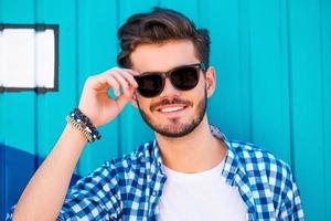 casualmente bello. contento giovane uomo regolazione il suo occhiali e sorridente mentre in piedi all'aperto foto