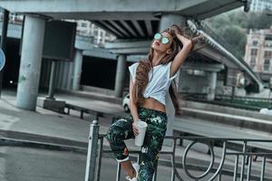 città ragazza. bellissimo giovane donna conservazione mano nel capelli mentre Tenere un' monouso tazza all'aperto foto