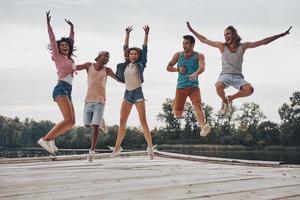 godendo loro libertà. pieno lunghezza di giovane persone nel casuale indossare sorridente e Esprimere a gesti mentre salto su il molo foto