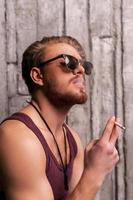 freddo bello fumare. lato Visualizza di bello giovane uomo nel occhiali da sole fumo un' sigaretta foto