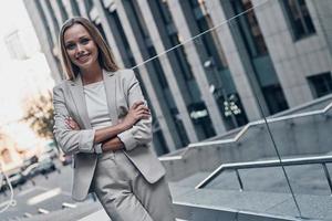 ritratto di fiducia. bellissimo giovane donna nel completo da uomo guardare a telecamera e sorridente mentre in piedi all'aperto foto