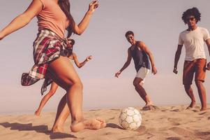 spiaggia divertimento. gruppo di allegro giovane persone giocando con calcio palla su il spiaggia foto